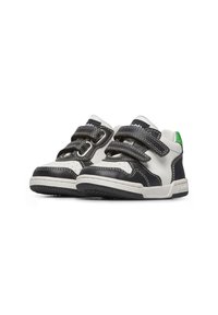 Sneaker in bianco e nero con dettagli perforati, doppie fascette in Velcro, suole in gomma e un accento verde sul tallone. Design robusto e basso.