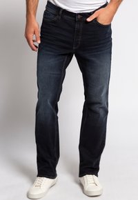 Jeans in denim blu scuro con taglio dritto, caratterizzati da un leggero sbiadimento, cuciture a contrasto, cinque tasche e chiusura con bottone, abbinati a sneakers bianche.