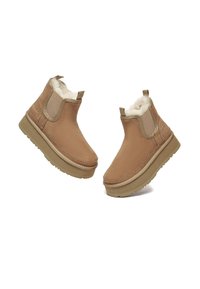 Beige Wildleder-Stiefeletten mit Fellfutter, elastischen Seiteneinsätzen und Gummisohle. Glatte Textur mit flachem, gepolstertem Fußbett.