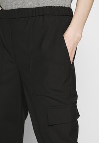 Zwarte cargobroek met een elastische tailleband, voorzien van zijzakken en zichtbare stikseldetails. Gemaakt van een gladde, lichte stof.