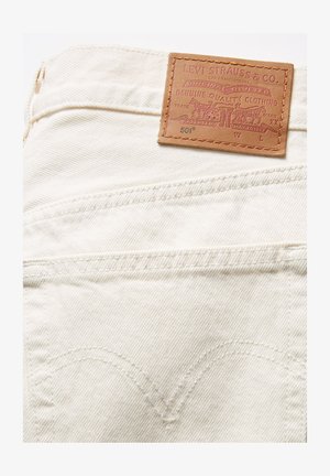 Denim bianco con etichetta in pelle con testo in rilievo, incluso "LEVI STRAUSS & CO.", e cuciture dettagliate sulle tasche posteriori.