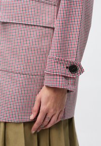 Κόκκινο και λευκό καρό σακάκι με δομημένο σχέδιο, λεπτομέρεια με κουμπωτά μανίκια και λεία υφή.