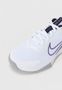 Baskets Nike Air Max blanches et violettes avec empeigne en mesh, lacets blancs et semelle grise sur fond blanc.