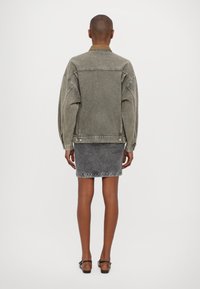 Person standing facing away wearing a faded gray denim jacket, matching gray denim skirt, and black flat shoes with ankle straps.