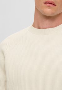 Crème ribgebreide trui met een ronde halslijn en raglanmouwen, met een gestructureerd stoffenpatroon en een gladde afwerking.