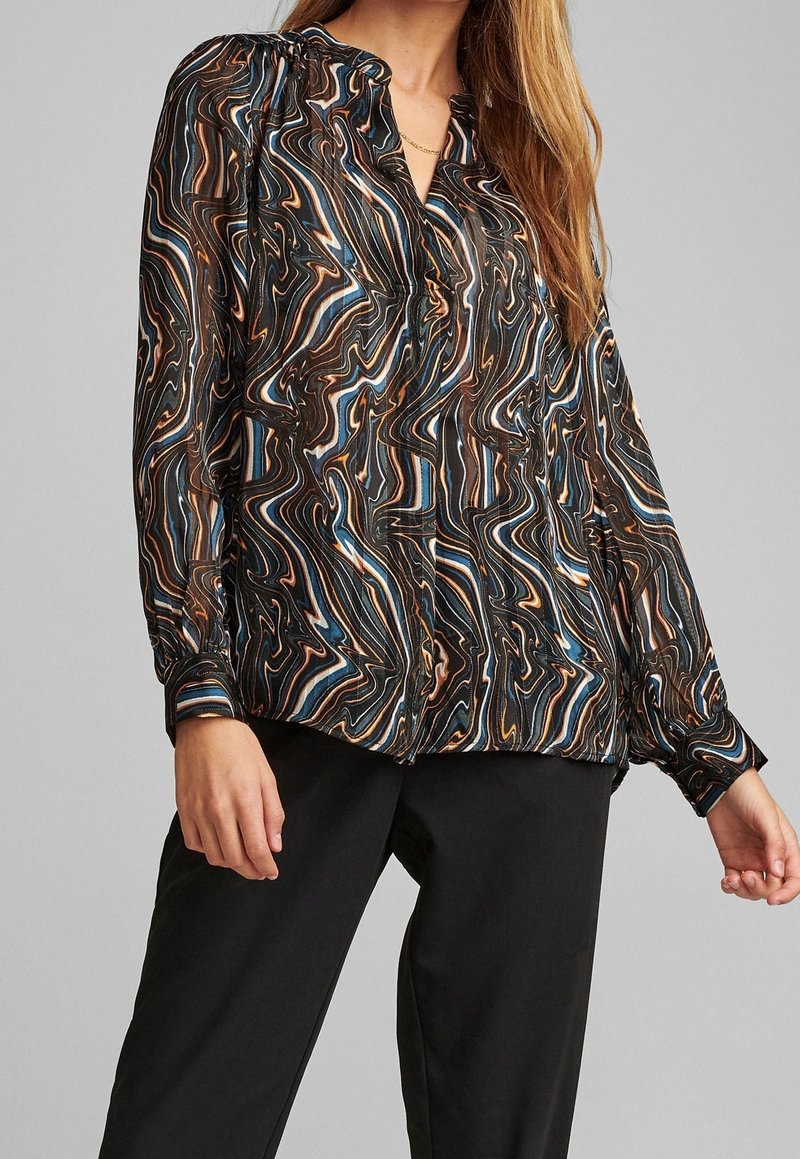 Blusa a fantasia fluida in nero, marrone e blu, con chiusura a bottoni frontale, leggermente a sbuffo e realizzata in un tessuto morbido e leggero.