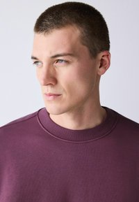 Lila pulóver bordázott nyakkivágással, sima, texturált anyagból, testhezálló kialakítással és minimalista stílussal.