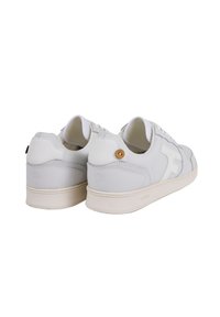 Une paire de baskets blanches basses avec des semelles beiges et un détail en bouton en bois sur le talon, présentée de l'arrière et en angle.