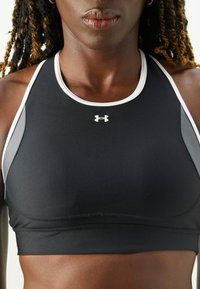 Svart treningstop med hvit kant og grå detaljer, laget av elastisk stoff med en tettsittende design. Under Armour-logoen er plassert midt på framsiden.