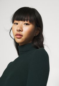 Mörkgrön ribbad polotröja med en figurnära passform. Tyget ser mjukt ut med en subtil textur.