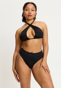 Ensemble de bikini noir comprenant un haut à col halter avec une découpe en forme de trou et un bas taille haute. Fabriqué en tissu lisse et extensible.