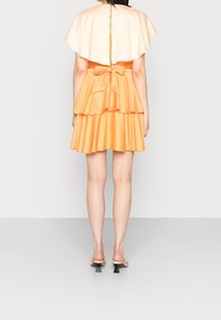 Robe en satin pêche avec une jupe à volants et un nœud à la taille, associée à un haut sans manches et des sandales à talons hauts.