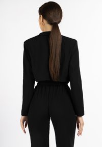 Sort jumpsuit med lange ærmer, tætsiddende talje og rynkede detaljer ved anklerne. Glat stof og minimalistisk design.