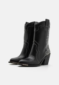 Botas de vaquero de cuero negro con costuras blancas, puntera afilada y acentos de estilo occidental. Tacón cuadrado y patrones decorativos en los costados.