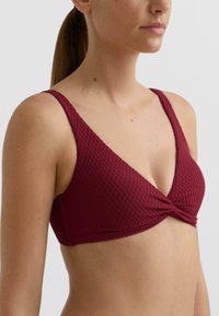 Bordowy top kąpielowy z fakturowanej tkaniny, miękki dekolt w kształcie litery V, szerokie ramiączka oraz skręcony przód dla dodatkowego efektu trójwymiarowości.