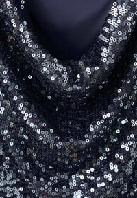 Tamnoplava tkanina za zavjese, prekrivena gustim srebrnim šljokicama koje odražavaju svjetlost, stvarajući teksturiranu površinu s blistavim učinkom.