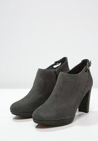 Grå mocka-ankelboots med hög, klumpig klack, rund tå, sidodragkedja och detalj med ankelsnodd för extra säkerhet.