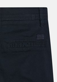 Pantaloni in cotone blu scuro con una tasca posteriore caratterizzata da cuciture orizzontali e un piccolo etichetta del marchio. Texture liscia e design su misura.