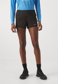  Sorte løbeshorts med en glat tekstur, elastisk talje og logo-detalje. Matcher med en blå langærmet bluse og sorte sko.