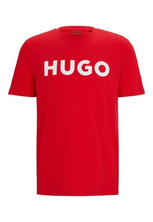 T-shirt en coton rouge avec un col rond et des manches courtes. Le devant arbore un logo "HUGO" blanc bien visible. Texture lisse.
