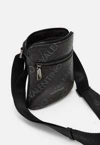 Svart Valentino crossbody-väska med flera dragkedjor, logotryck över hela ytan och justerbar axelrem med Valentino-märkning.