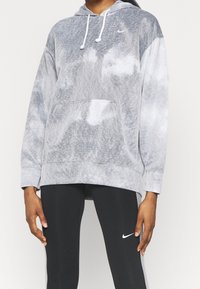 Jasnoszary dresowy hoodie w tie-dye z obszyciem, kieszenią z przodu i białym logo Nike. Noszony na czarnych legginsach, podkreślając swobodny, sportowy styl.