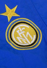 Blauwe stof met een gele en zwarte cirkelvormige sportembleem en een enkele gele ster geborduurd erboven.