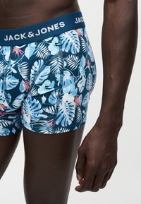 Άτομο που φορά μπλε μπόξερ Jack & Jones με τροπικό μοτίβο φύλλων· το χέρι του κρέμεται στο πλάι, απεικονίζεται από τη μέση μέχρι το μέσο του μηρού.
