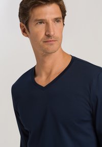 Granatowa bluzka z długim rękawem i dekoltem w serek, wykonana z gładkiego materiału, charakteryzująca się minimalistycznym designem bez widocznych wzorów czy dodatków.