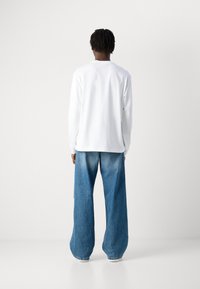 Langermet hvit skjorte med avslappet passform, kombinert med vide lyseblå denimjeans, med en falmet tekstur og rå kanter.