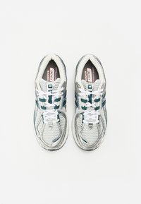 Hvite joggesko med tealfargede detaljer, mesh-overdel og hvite lisser. Har polstret krage og teksturert gummi såle. Modellenummer synlig.
