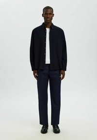 Granatowa koszula zapinana na guziki noszona na białej koszulce, w połączeniu z ciemnymi spodniami i czarnymi butami. Prosty krój i luźny fason. Gładka tekstura materiału.