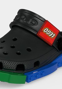 Μαύρο τσόγκ με τρύπες αερισμού, κόκκινο λουράκι με το λογότυπο LEGO και μπλε και πράσινες λεπτομέρειες στη σόλα εμπνευσμένες από τουβλάκια LEGO.