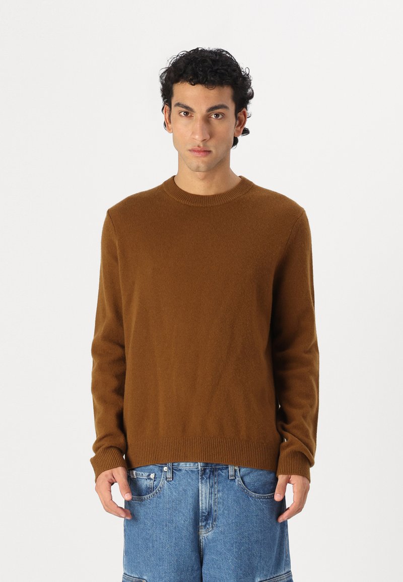 Pull en maille brun avec des manches longues, col ras du cou et ourlet côtelé, associé à un short en denim bleu. Texture douce, design décontracté.