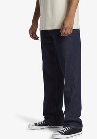 Mörkblå denimjeans med rak benpassform, med en subtil textur och fickor. Tillsammans med svarta och vita sneakers.