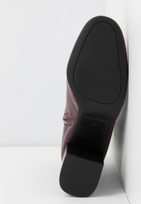 Semelle d'une botte en cuir bordeaux avec talon et semelle en caoutchouc noir, taille 37, présentée debout contre un fond d'angle blanc.