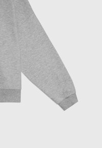 Szary rękaw bluzy z gładką fakturą, ściągacz na mankiecie i lekko oversize'owy krój. Materiał wydaje się miękki i wygodny.