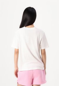 Hvid bomulds t-shirt med korte ærmer, rund halsudskæring og afslappet pasform, parret med rosa shorts, set fra bagsiden.