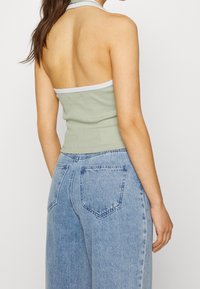 Světlězelený pruhovaný halter crop top s bílým lemem, spárovaný s volnými modrými denimovými džíny s zadními kapsami a vybledlou texturou.