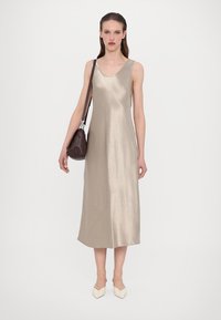 Satin beige ermeløs kjole med V-hals, kne-lengde hem, glatt tekstur, kombinert med en mørkebrune veske og kremfargede spisse sko.