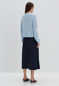 Un pull en tricot bleu clair avec un design court et un ourlet côtelé, associé à une jupe midi bleu marine. Tissu lisse et coupe décontractée.