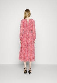 Robe rouge mi-longue avec un motif de rayures zèbre, des manches longues, une taille cintrée et un détail de dos en forme de trou de serrure. Portée avec des sandales à talons noires.