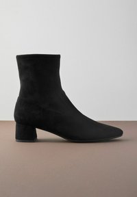 Bottines en daim noir avec un bout pointu et un talon carré bas, offrant une construction sans couture et une texture lisse.