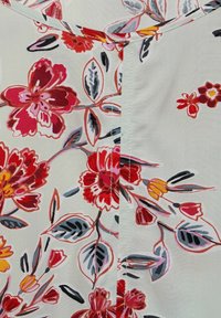 Blommig tyg med stora röda och rosa blommor på en krämfärgad bakgrund. Inkluderar gröna blad och svarta accenter. Sömdetalj synlig.