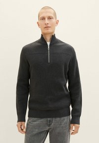 Dunkelgrauer gestrickter Pullover mit hohem Kragen und halberReißverschluss, der über strukturierte Rippen an den Schultern und eine taillierte Silhouette verfügt.