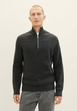 Mørkegrå strikket sweater med høj krave og halvlukning, der har ribbet tekstur på skuldrene og en tætsiddende silhuet.