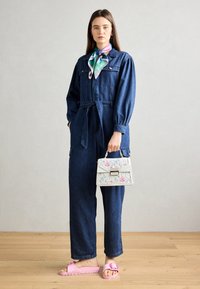 Denim-hyppytakki, jossa on solmittava vyötärö, pitkät hihat ja taskut. Yhdistetty valkoiseen kukkakuosiseen käsilaukkuun ja vaaleanpunaisiin liukusandaaleihin. Sileä pinta.