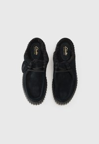 Sorte semsket slip-on sko med faux fur foring, med en teksturert yttersåle og dekorative snørebånd. Innvendig merket "Clarks Signature."