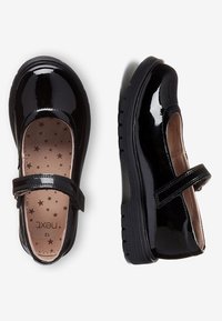 Black patent leather Mary Jane shoes with Velcro straps, star-patterned beige insoles, and sturdy rubber soles, shown from top and side views.