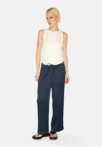 White sleeveless top and navy wide-leg trousers with a drawstring waistband, featuring a textured fabric and flat sandals.